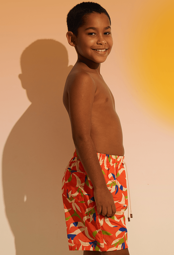 Menino de perfil usando bermuda infantil laranja com estampa colorida e cós elástico