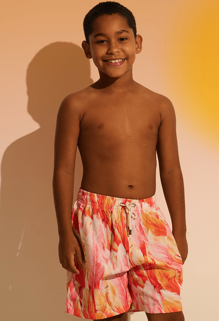Menino sorridente vestindo Bermuda Beach Infantil Brisa Doce em tons de rosa, vermelho e laranja