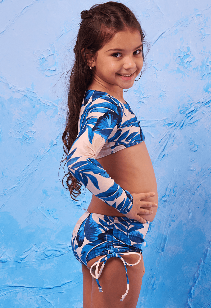 Menina criança posando de perfil direito, sorrindo, vestindo biquíni Valentina Terra Azul