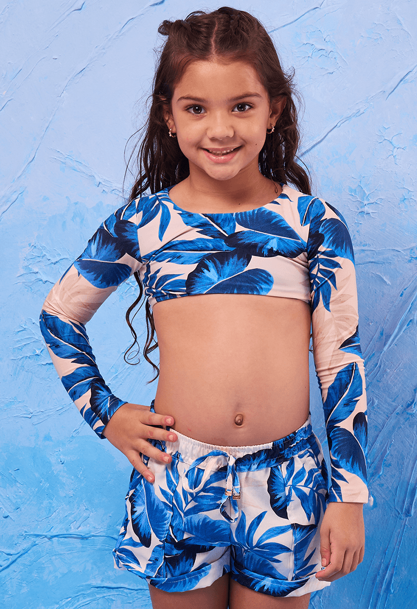 Imagen frontal de menina vestindo short infantil estampado de folhas azuis sobre fundo bege