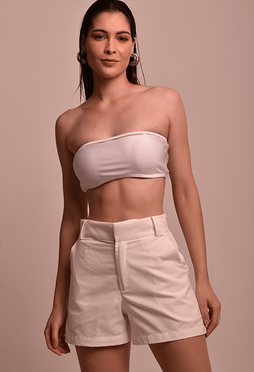 Modelo feminina usando short branco de tecido liso com caimento reto e cintura alta, apresentando pregas frontais e bolsos laterais.