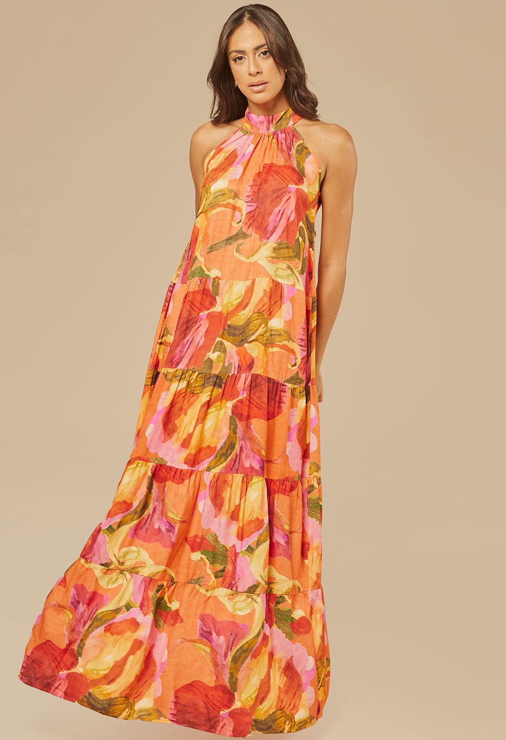 Modelo usando Vestido New Jasmin Chamego com estampa floral em tons de laranja, rosa, vermelho, amarelo e verde, gola halter e camadas franzidas
