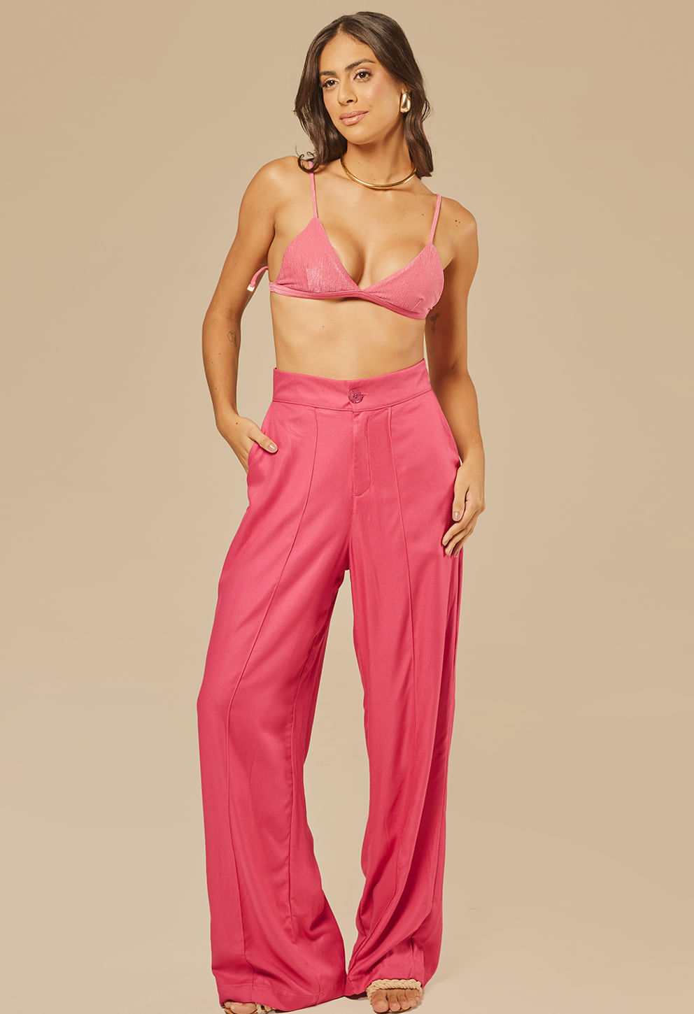 Modelo usando calça pantalona rosa vibrante com cintura alta e bolso nas laterais, pregas frontais, botão e zíper