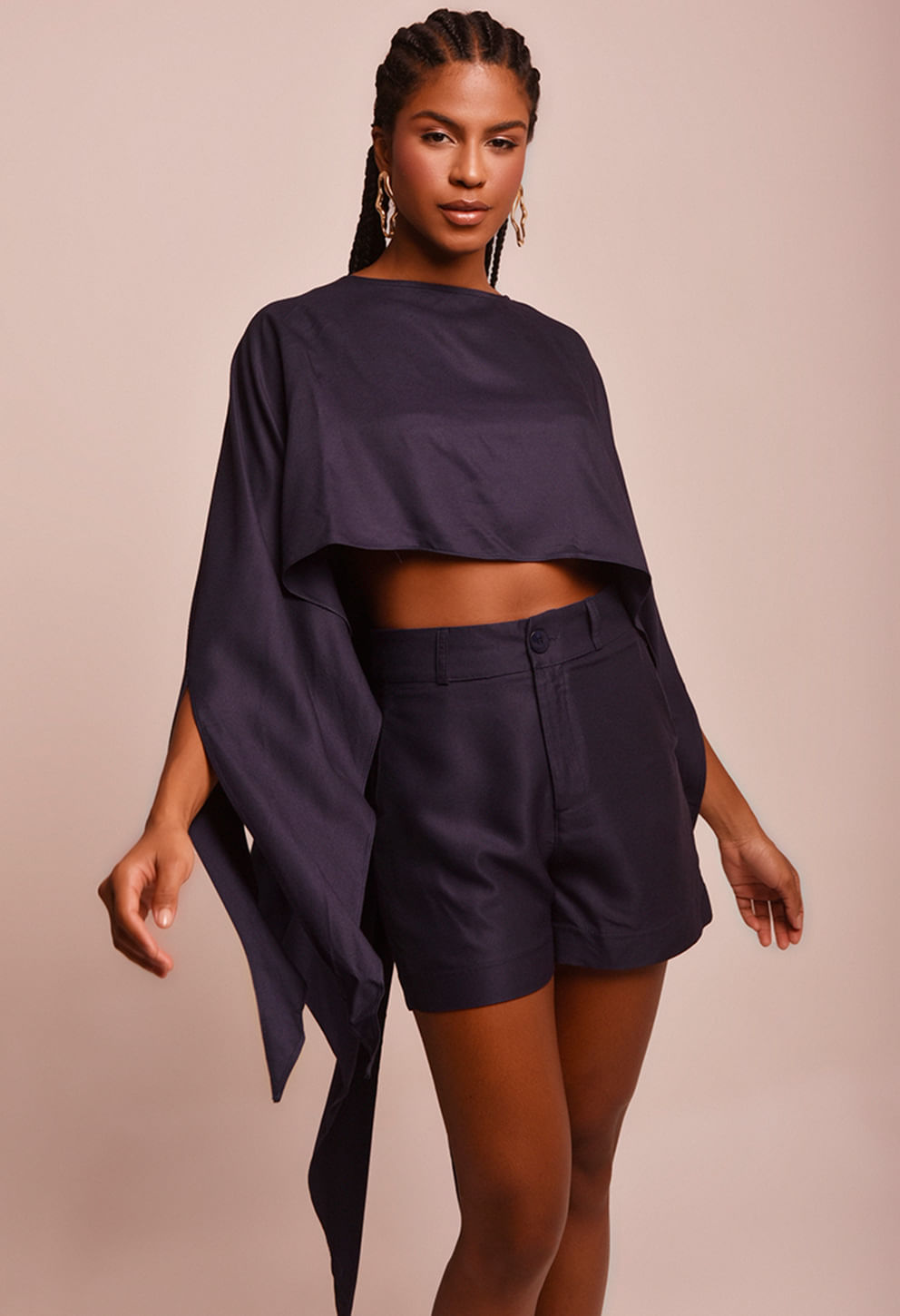 Modelo feminina vestindo blusa cropped azul marinho escuro com caimento fluido e mangas longas assimétricas que formam pontas