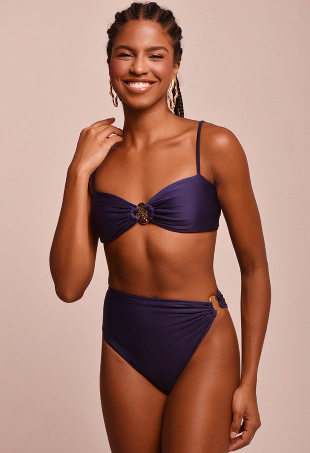 Modelo sorrindo usando top faixa com alças finas e medalha circular frontal em metal, cor roxo escuro/azulado.