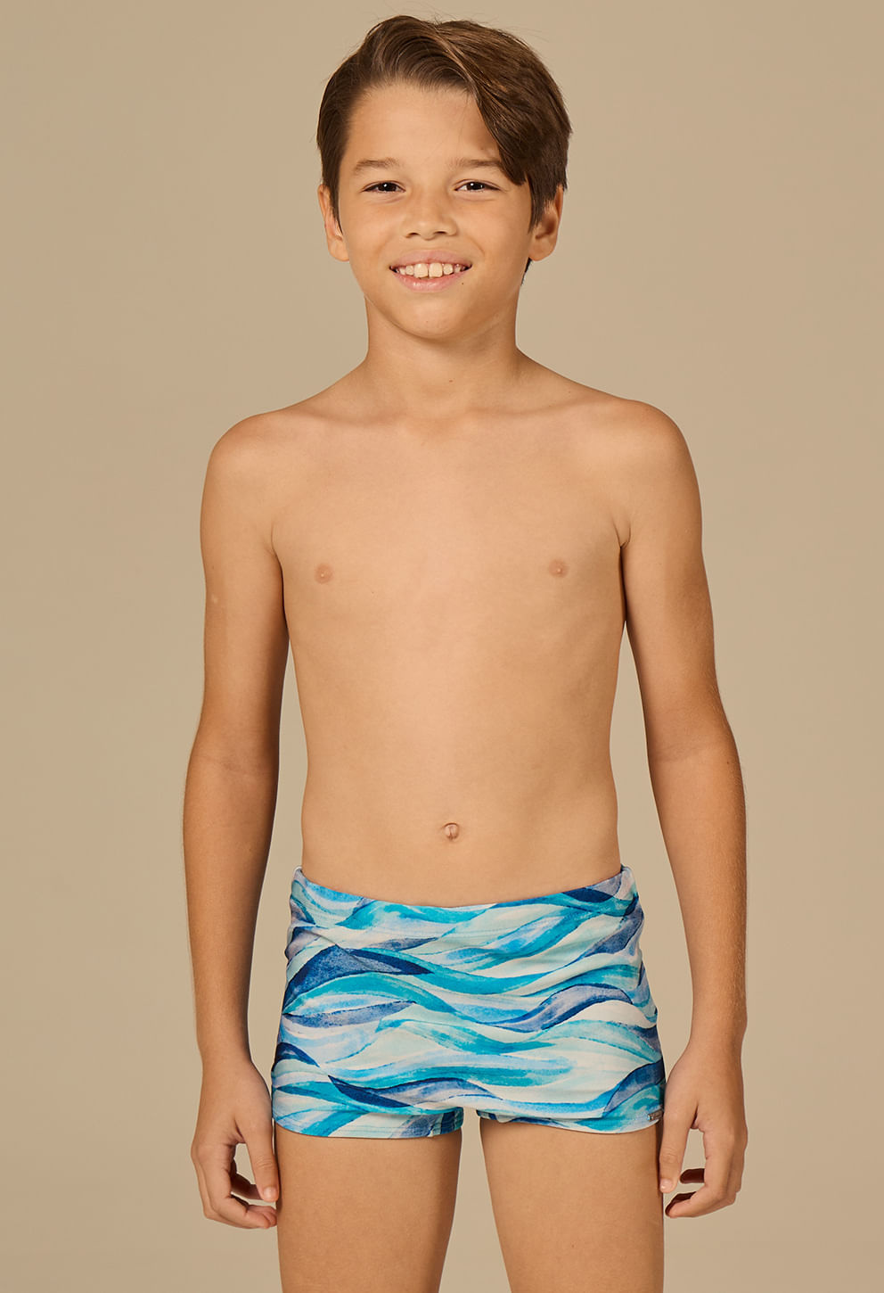Menino posando de frente, vestindo sunga short infantil em ondas azul claro, azul escuro e branco
