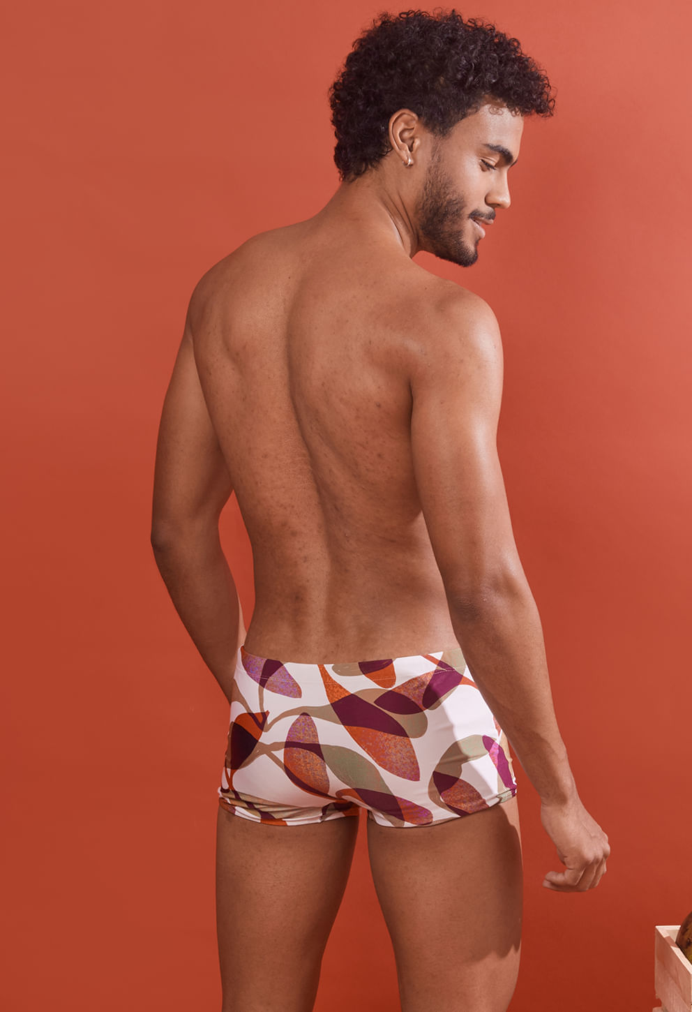 Vista traseira do modelo masculino vestindo sunga short adulto com estampa abstrata em branco, laranja, roxo, verde e bege