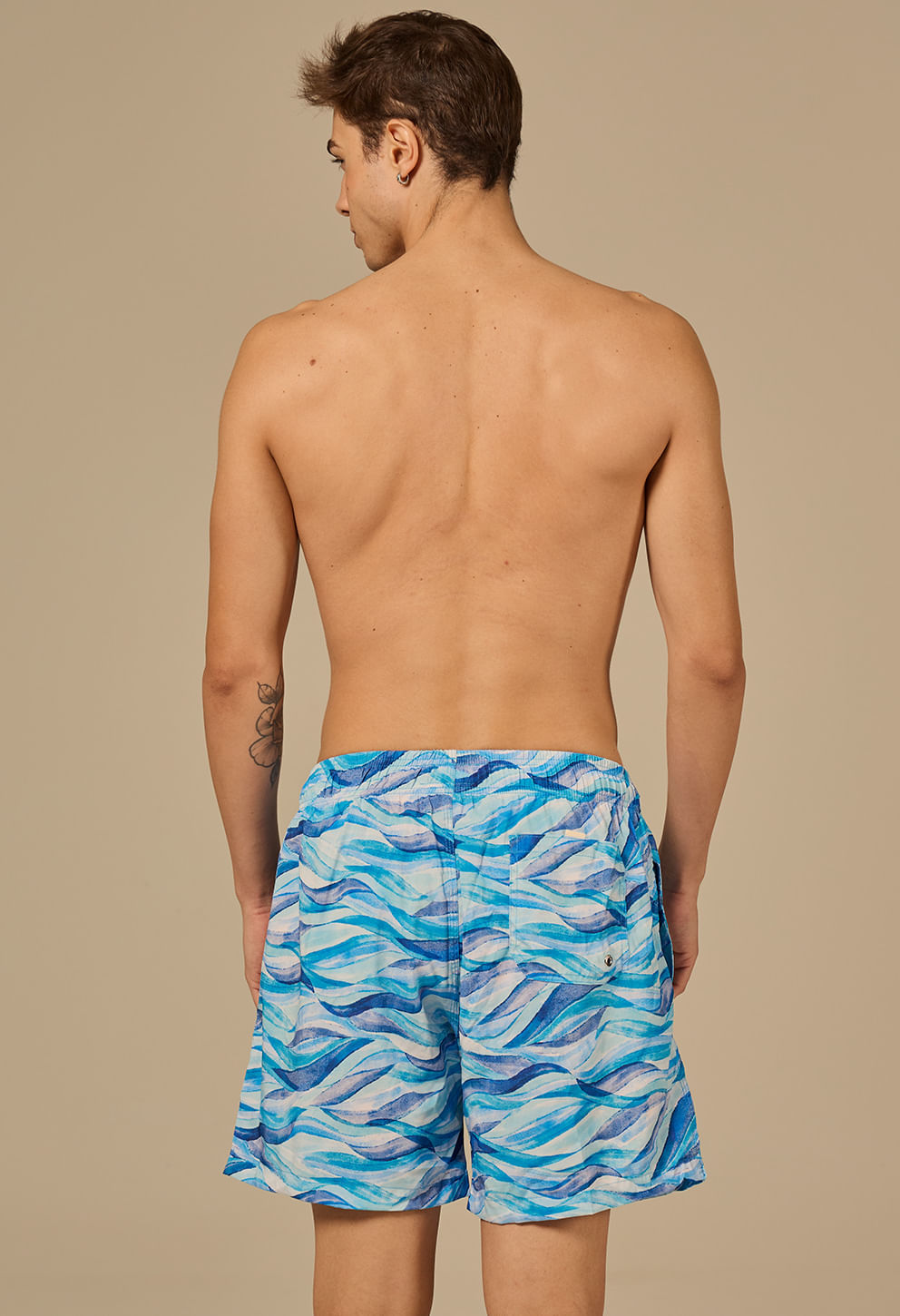 Modelo masculino visto de costas usando bermuda Orla azul com estampa de ondas e bolso traseiro.
