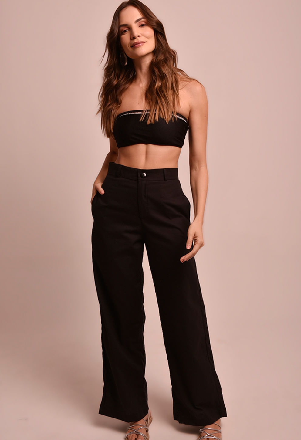 Modelo feminina em estúdio usando calça pantalona preta com cós alto e botões dourados