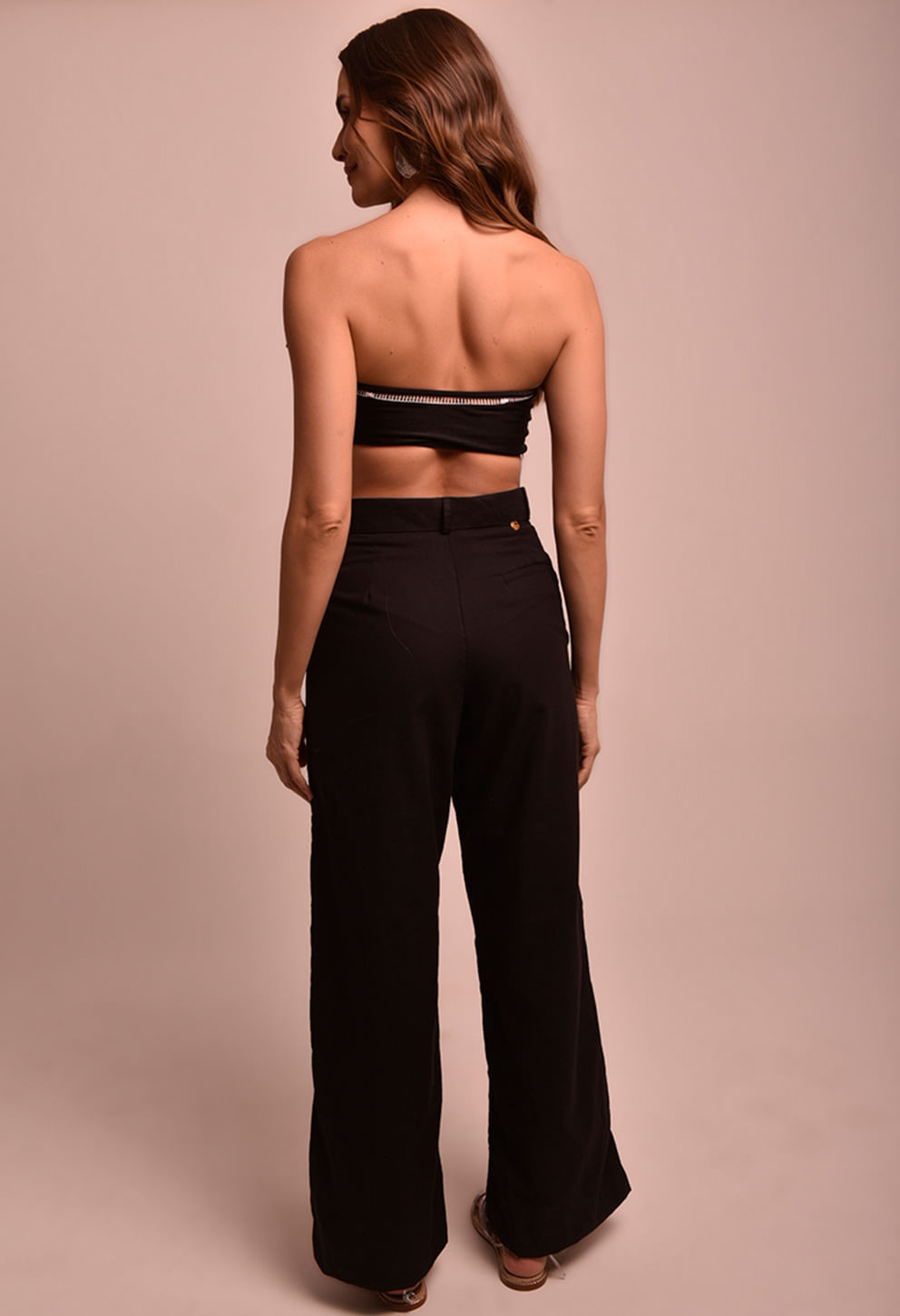 Vista traseira da calça pantalona preta com cós alto e detalhe de botão dourado