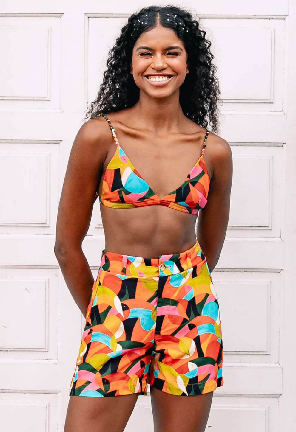 Modelo usando Short Lua Borogodó estampado vibrante, predominância laranja, cintura alta e botão dourado
