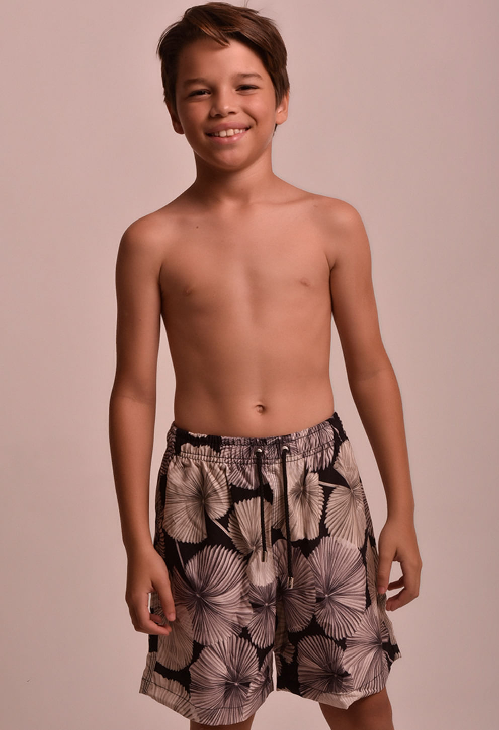 Menino sorridente vestindo bermuda infantil estampada em tons de cinza, preto e bege com cós elástico e cordão ajustável