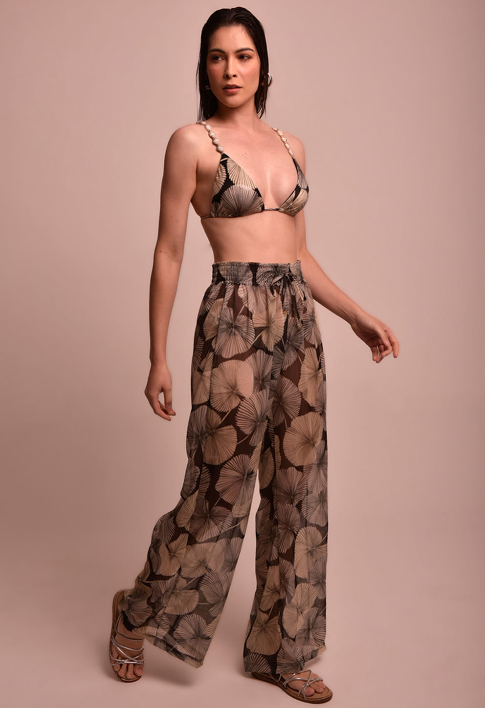Imagem frontal da calça pantalona estampada em folhas, mostrando comprimento longo que cobre parcialmente o calçado; caimento solto e cintura ajustada com elástico e cordão.
