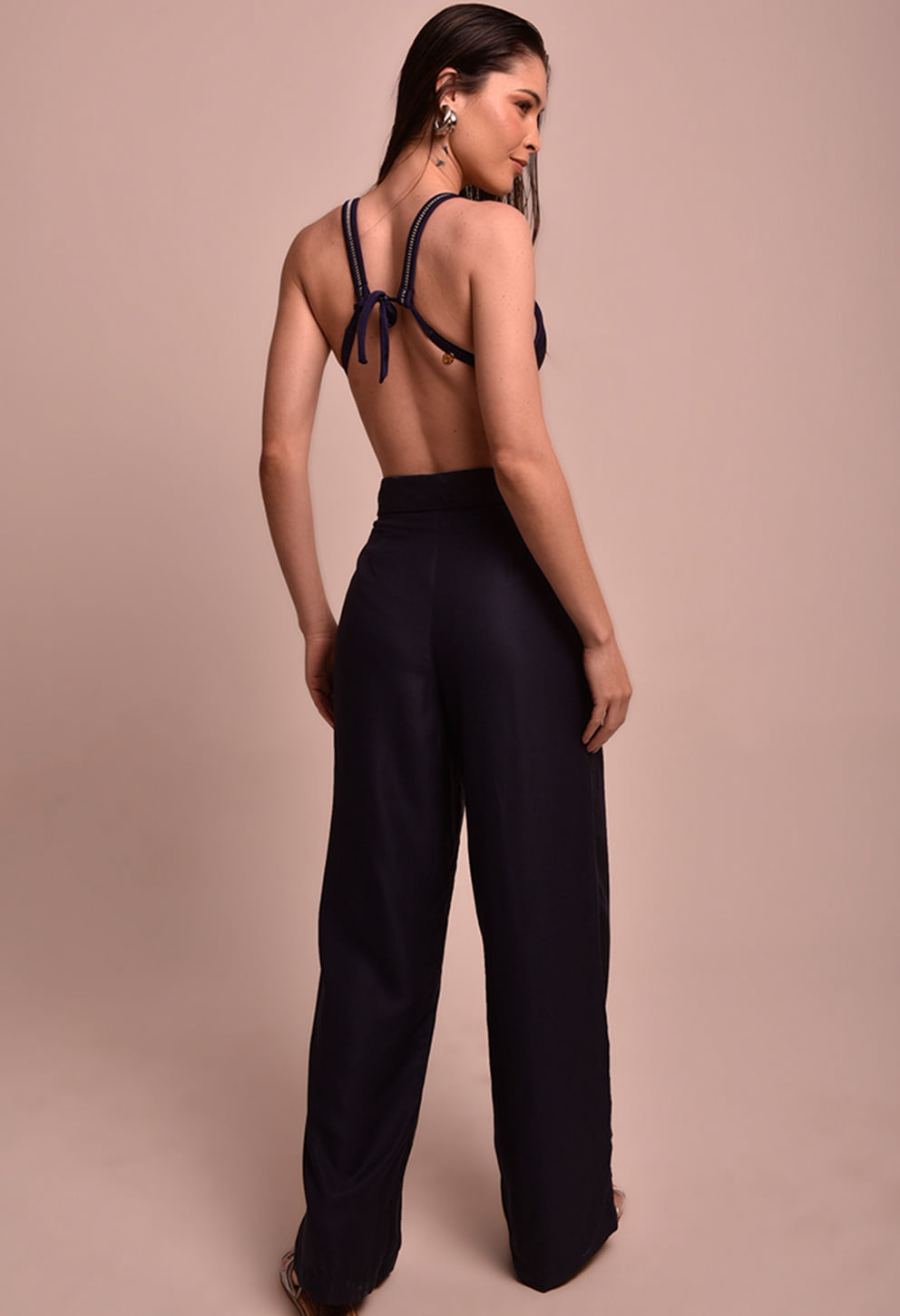Imagem traseira da modelo vestindo calça pantalona marinho, mostrando a cintura alta e o caimento largo da calça.