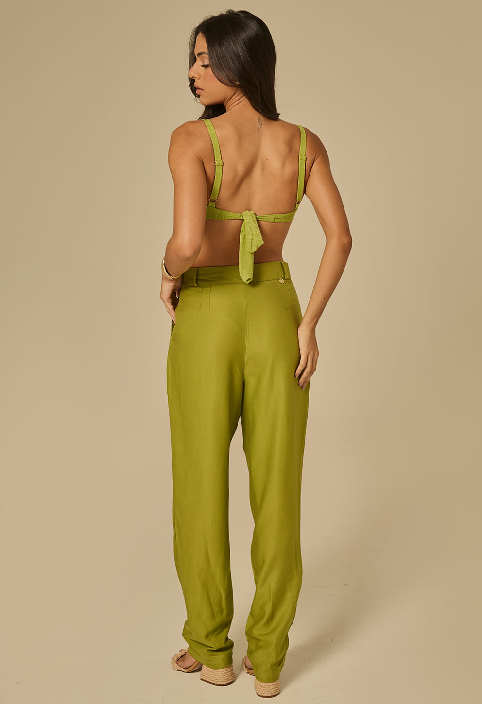 Modelo feminina vista de costas usando calça reta esmeral com cintura alta, passantes e acabamento liso nas costas; bolsos embutidos e caimento levemente solto.