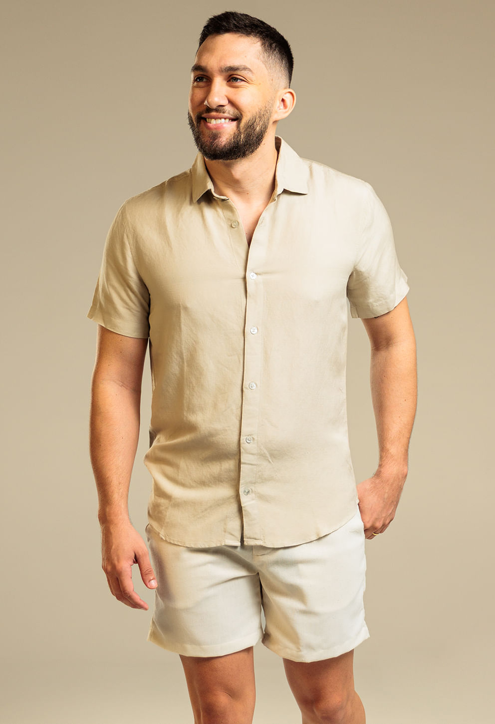 Modelo usando bermuda alfaiataria natural com camisa bege clara em estúdio