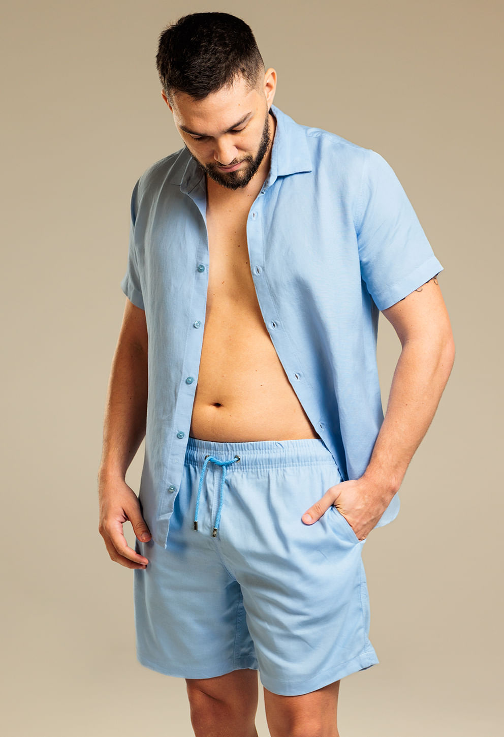Modelo masculino em pé usando bermuda casual e camisa de linho azul claro