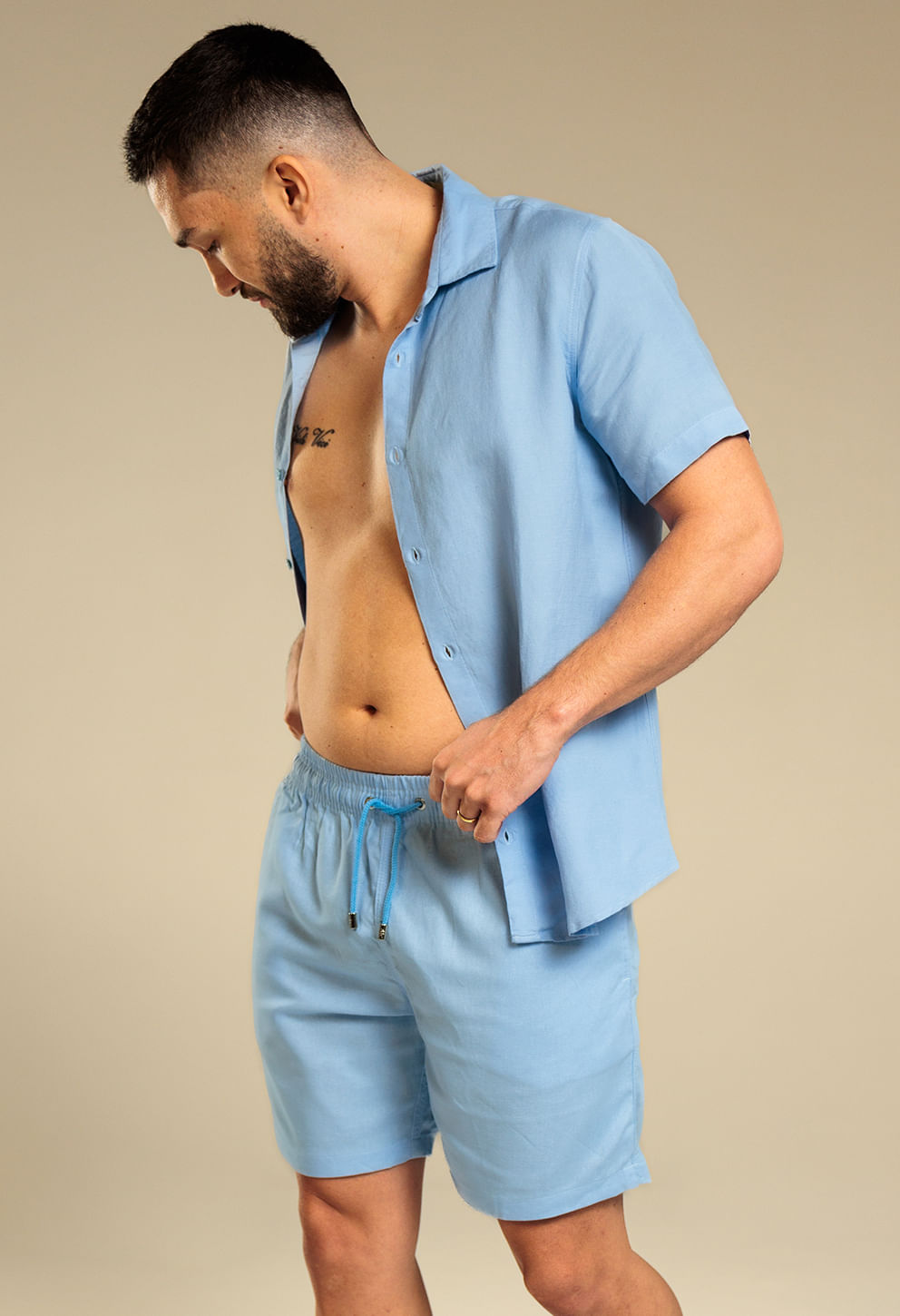 Visão lateral de modelo masculino com bermuda casual azul claro e camisa aberta