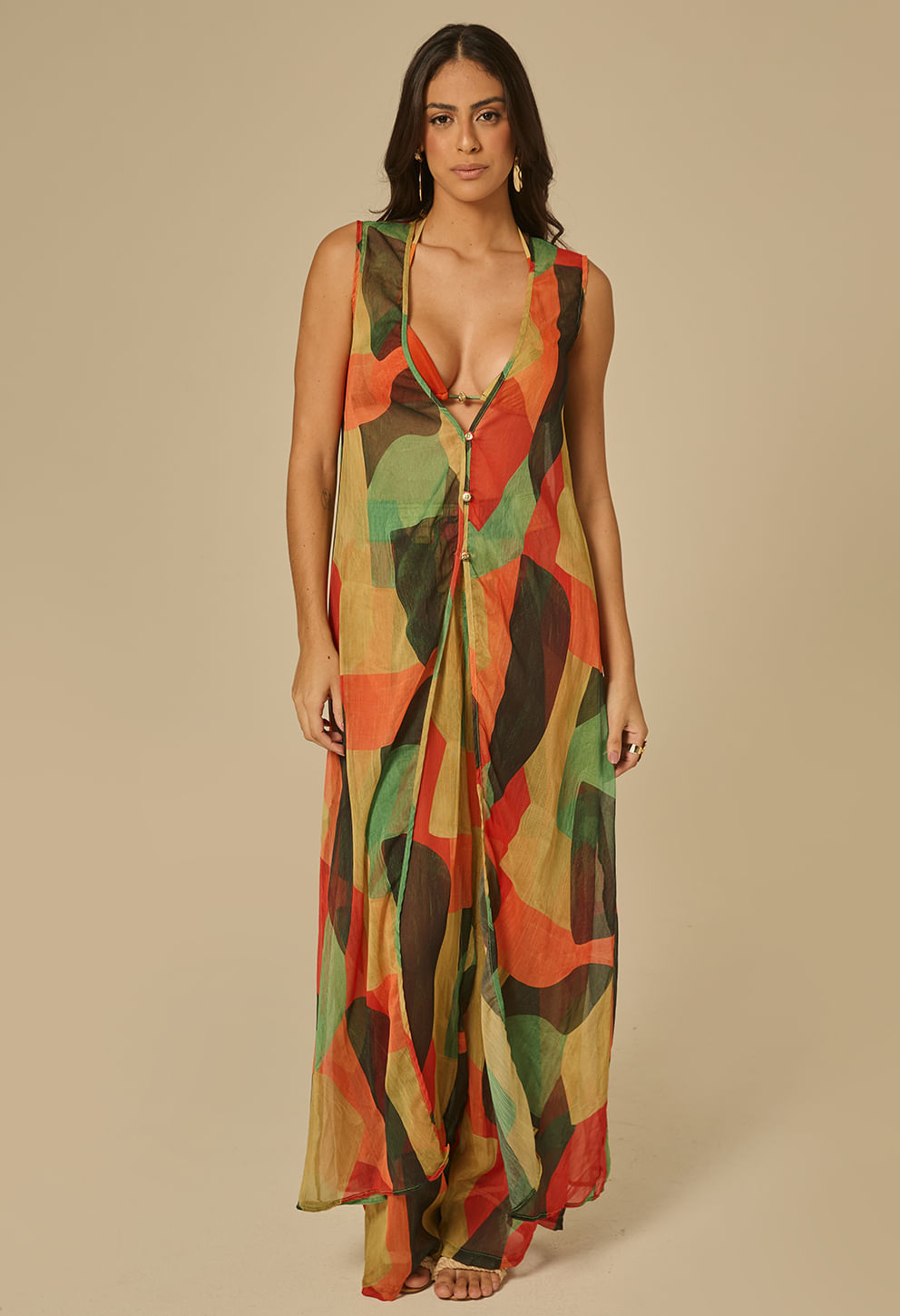 Modelo feminina em pé usando saída de praia longa e fluida com estampa geométrica multicolor (tons verdes, laranja, vermelho e marrom)