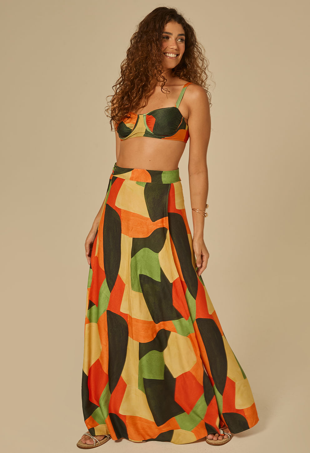 Modelo em leve movimento usando saia longa estampada geométrica multicolor (verde, laranja, preto, amarelo).