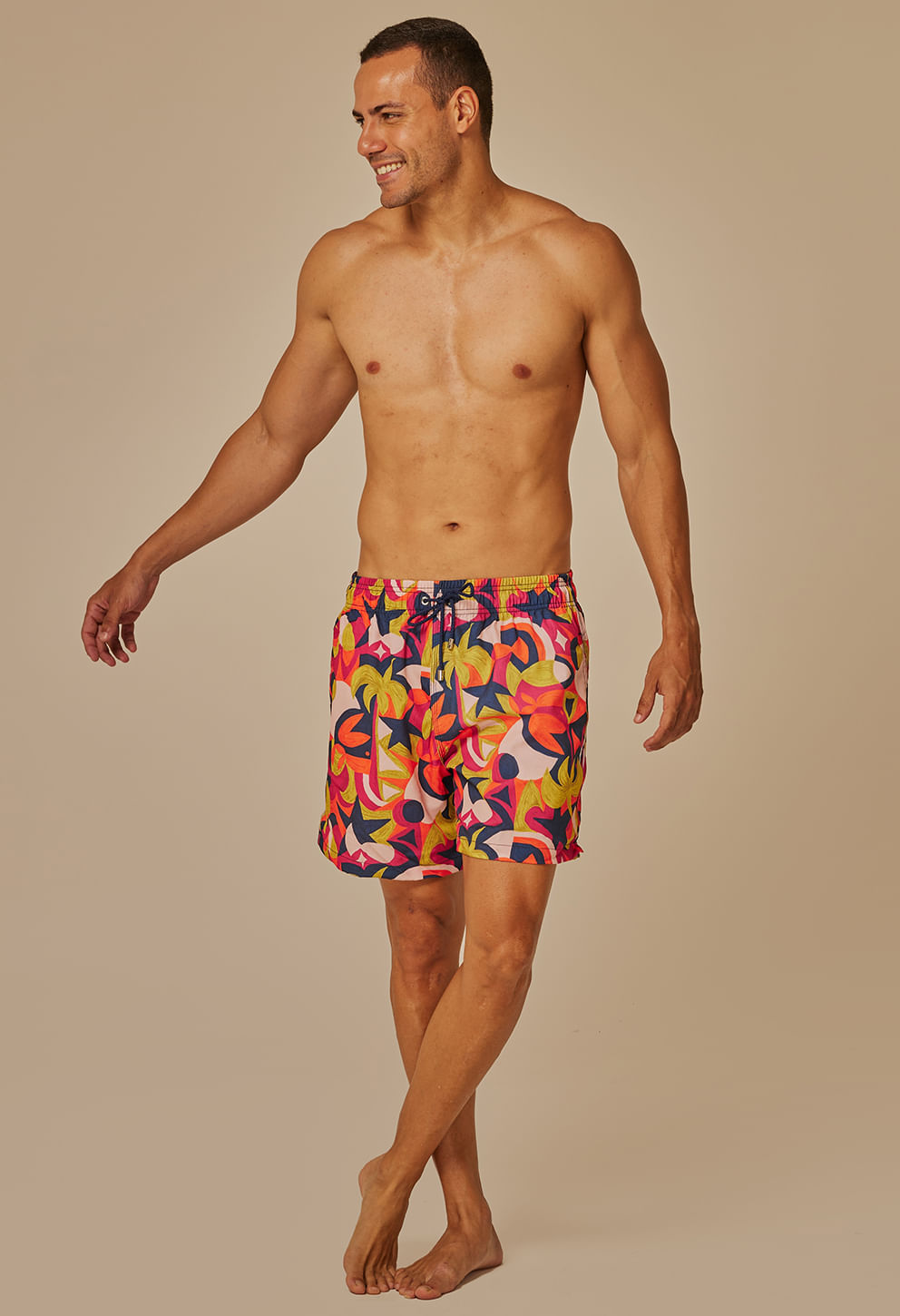 Modelo masculino usando bermuda casual shortinho Tropicália com estampa multicolor predominante rosa e laranja.