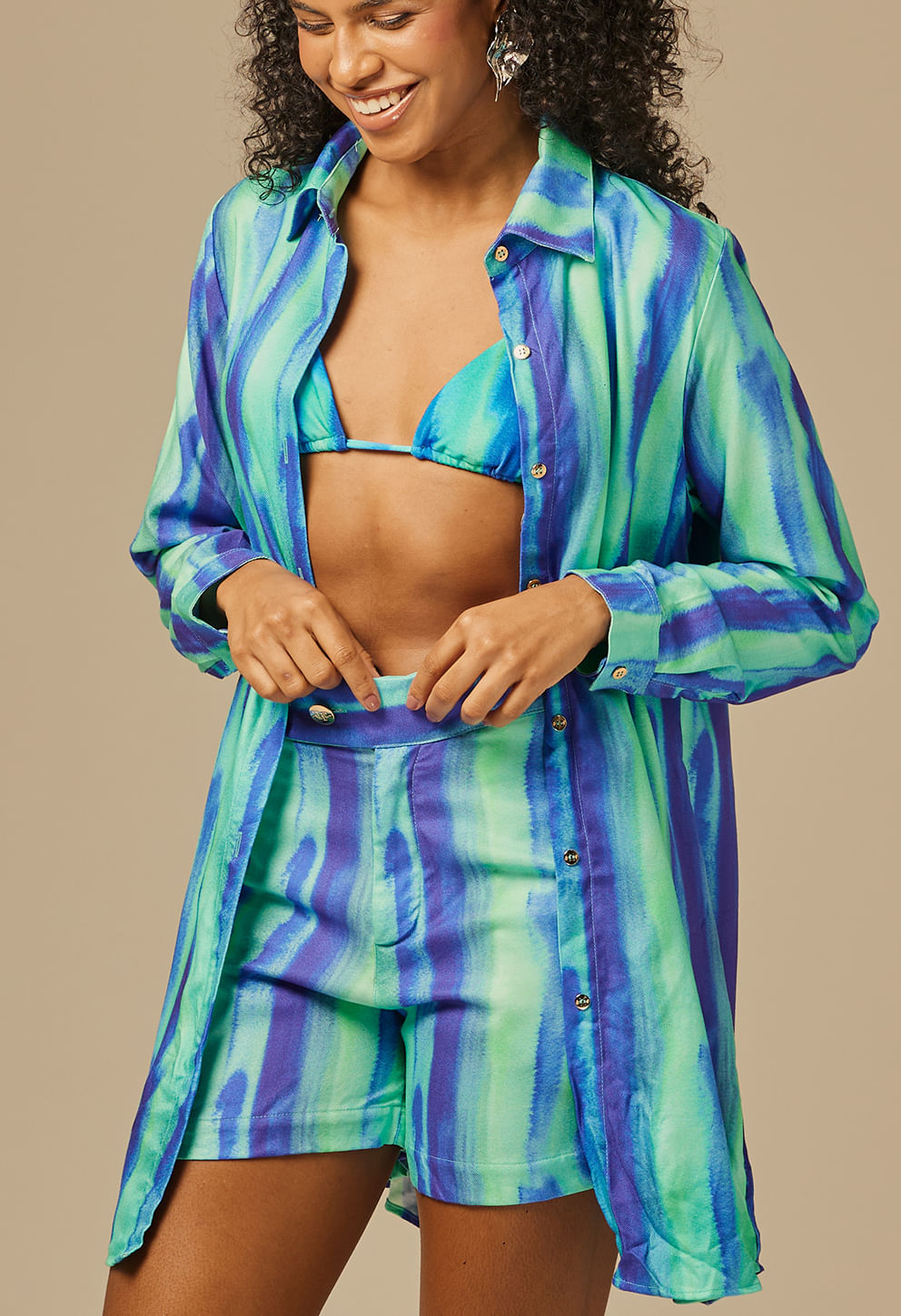 Camisão Boreal feminino com estampa listrada em tons de azul e verde, modelo sorrindo e ajustando o shorts