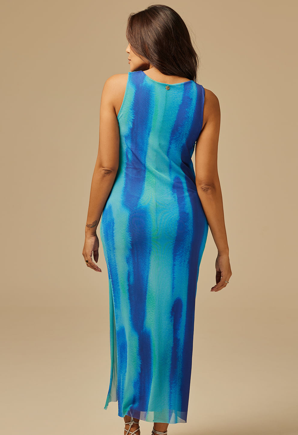 Vestido longo feminino sem mangas com estampa em tons de azul e verde, estilo tie-dye vertical, visto de costas com detalhe de botão dourado.