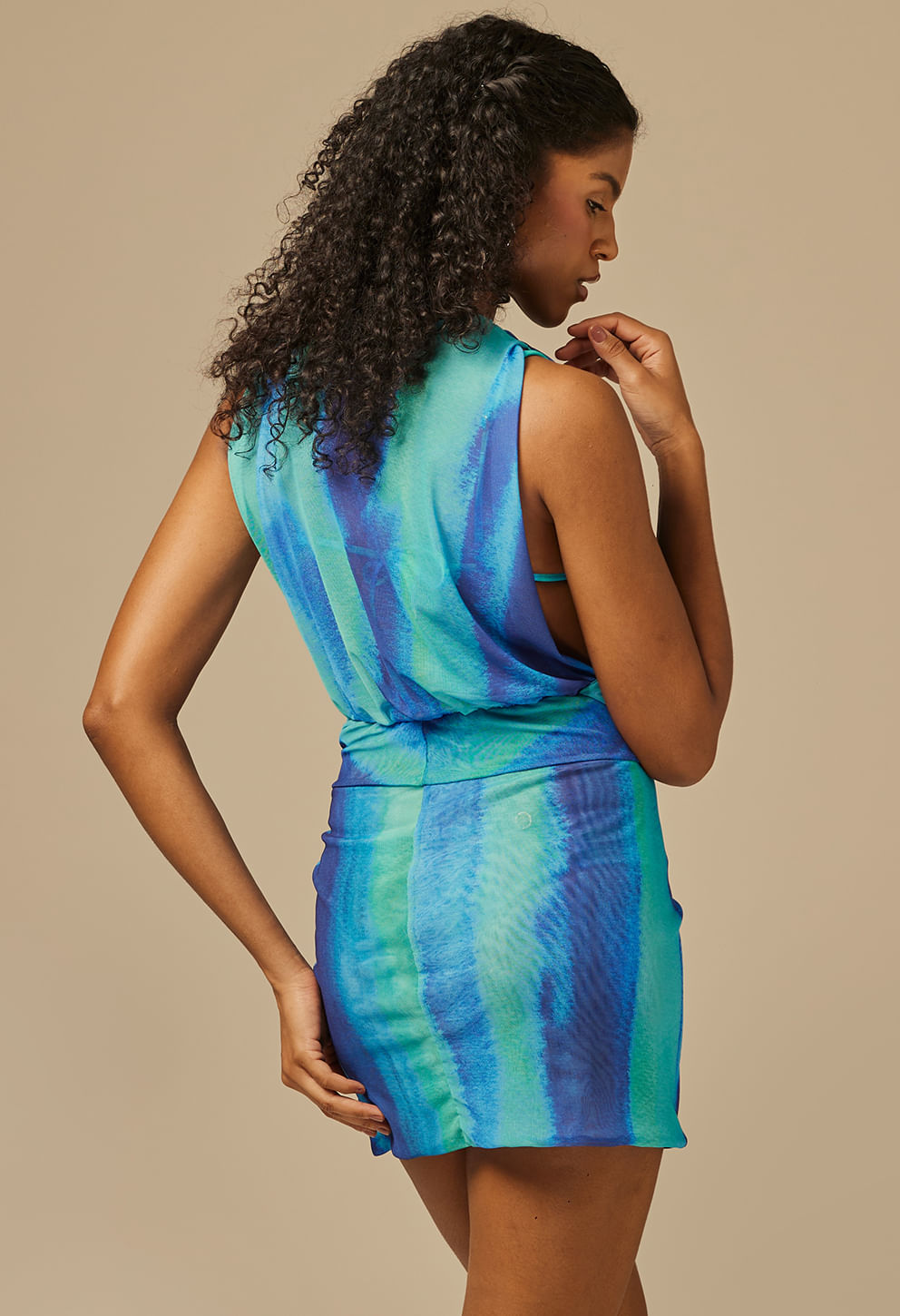 Vestido feminino Enora Boreal em azul e verde com padrão degradê, visto de costas. Modelo curto, sem mangas, com caimento justo e franzido lateral que cria um drapeado elegante. Decote profundo nas co