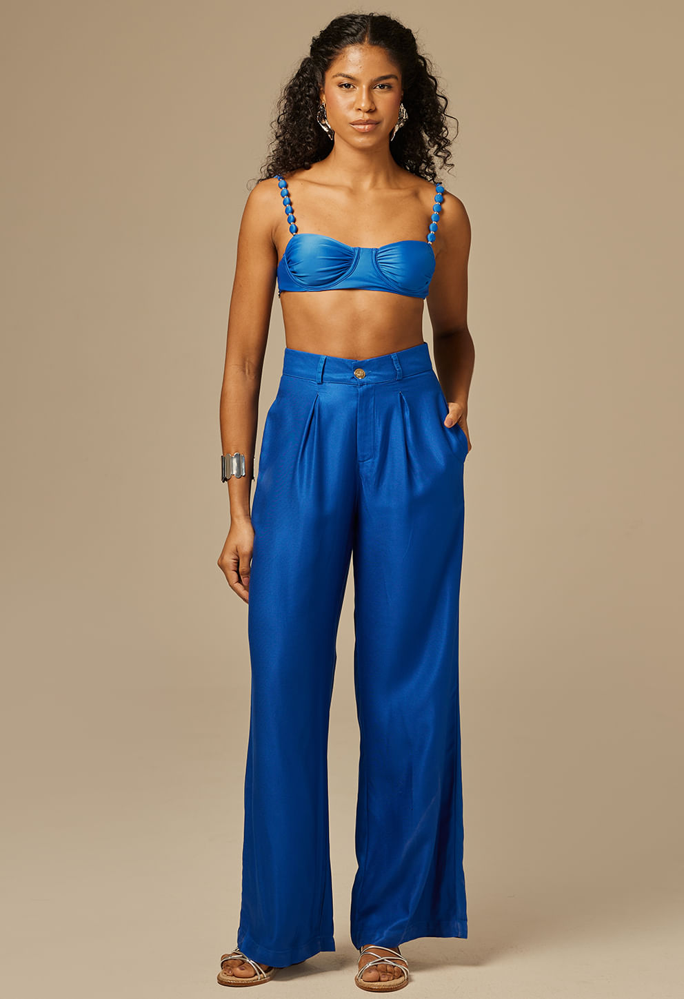 Modelo feminina usando calça pantalona social azul royal com cintura alta e pregas frontais