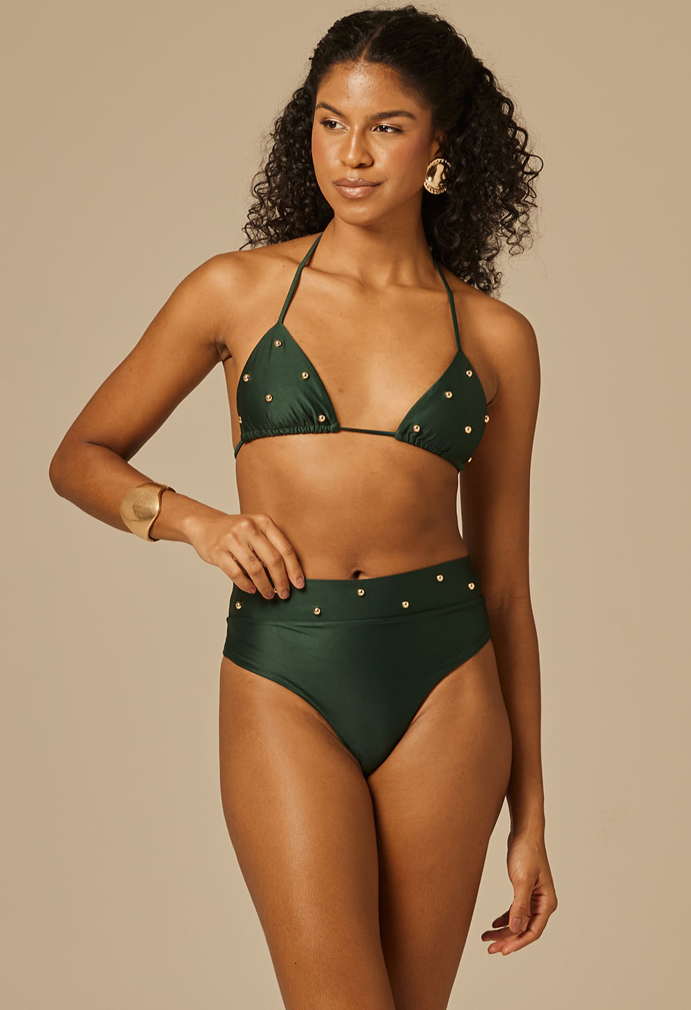 Mulher usando calcinha hot pant verde escuro com detalhes em ilhós dourados, vista frontal